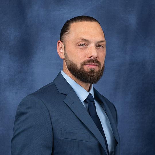 headshot of man with beard, in suit and tie